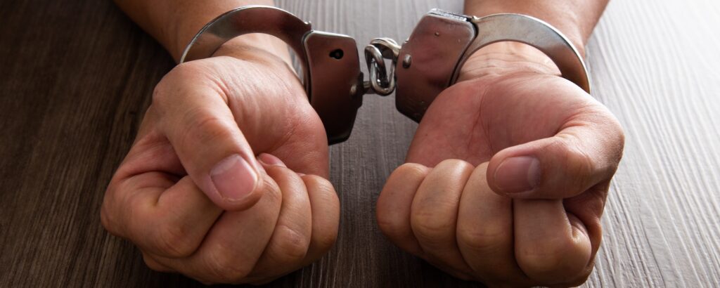 Arrested criminal hands locked in handcuffs.